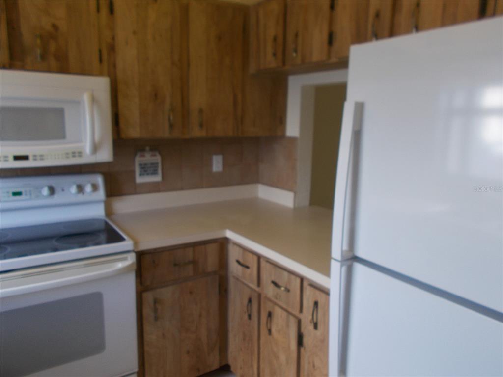 A kitchen features wood cabinets, white appliances, and a light-colored countertop — 2000 FORREST NELSON BOULEVARD UNIT C6, PORT CHARLOTTE, FL