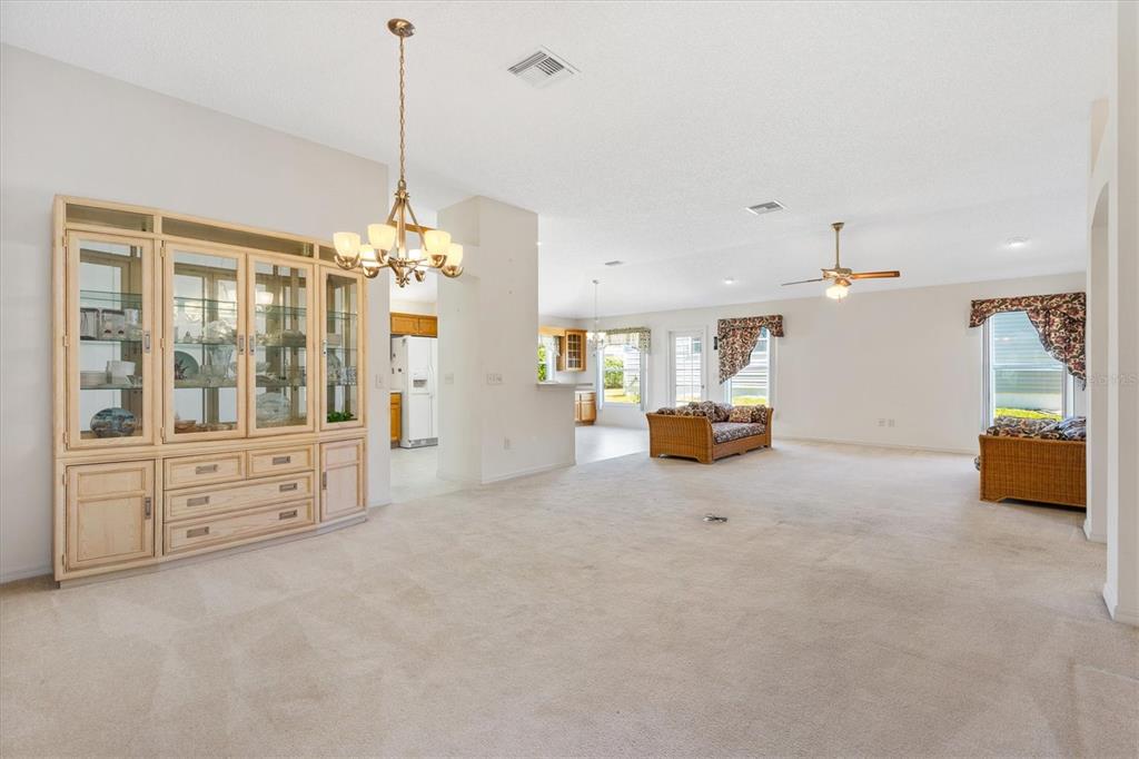 A spacious living room with beige carpeting, a large wooden hutch, and a ceiling fan — 17723 SE 81ST TIMBERWOOD TERRACE, THE VILLAGES, FL