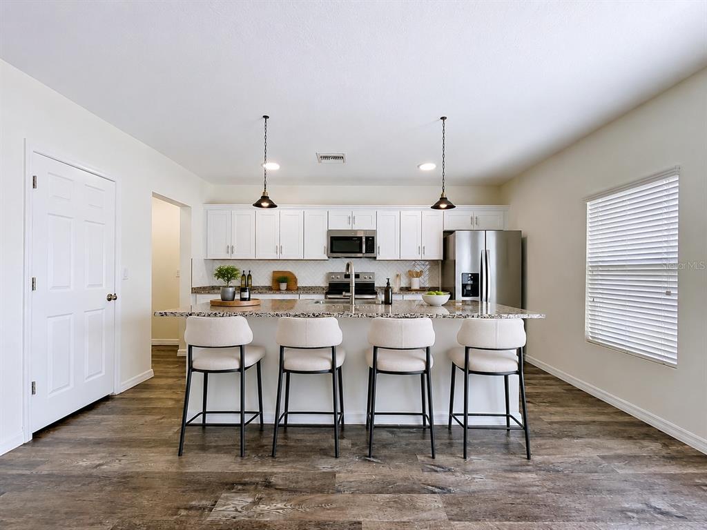 A modern kitchen features white cabinetry, granite countertops, a central island, and four bar stools — 1396 AXEL CIRCLE, WINTER HAVEN, FL