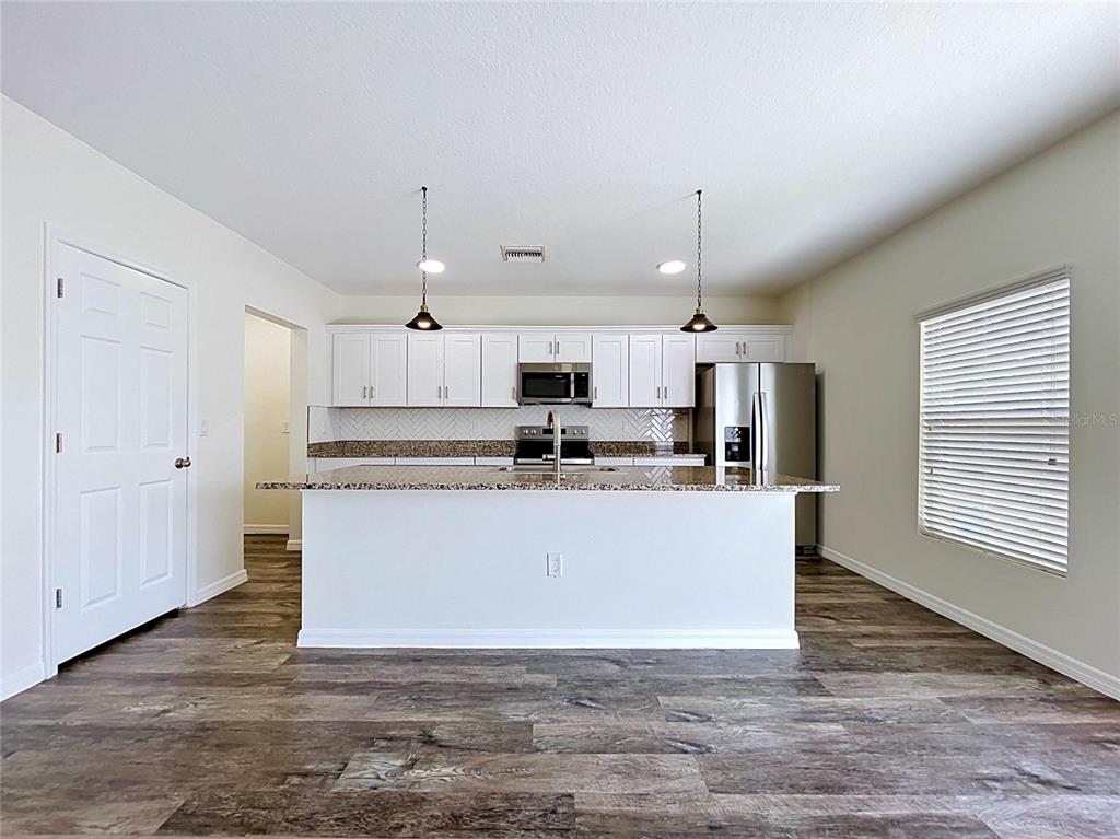 A kitchen features white cabinets, granite countertops, stainless steel appliances, and wood-look flooring — 1396 AXEL CIRCLE, WINTER HAVEN, FL