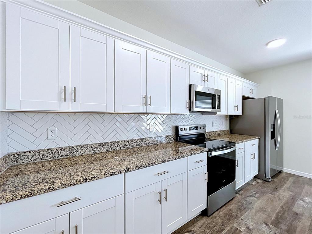 A kitchen features white shaker cabinets, granite countertops, a herringbone tile backsplash, and stainless appliances — 1396 AXEL CIRCLE, WINTER HAVEN, FL