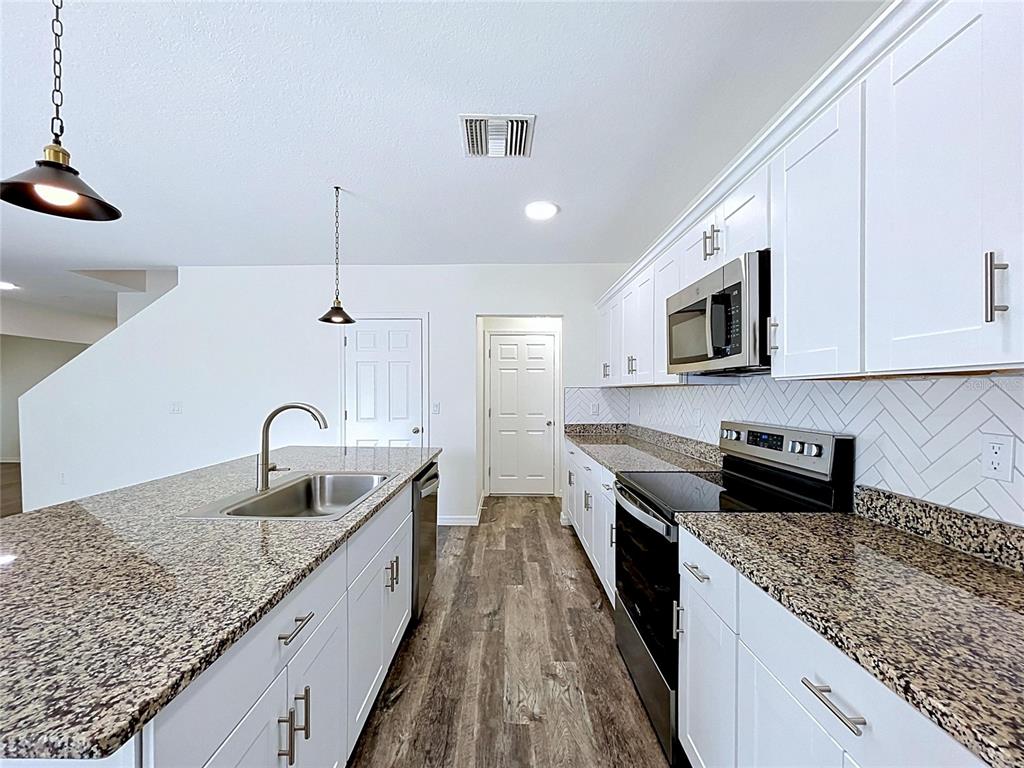 A kitchen features white cabinets, granite countertops, a herringbone backsplash, and a large island — 1396 AXEL CIRCLE, WINTER HAVEN, FL
