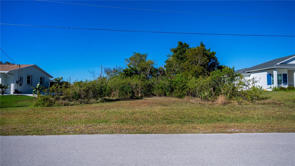 A vacant, grassy residential lot sits between two houses under a clear blue sky — 3013 CHAPMAN BOULEVARD, PUNTA GORDA, FL