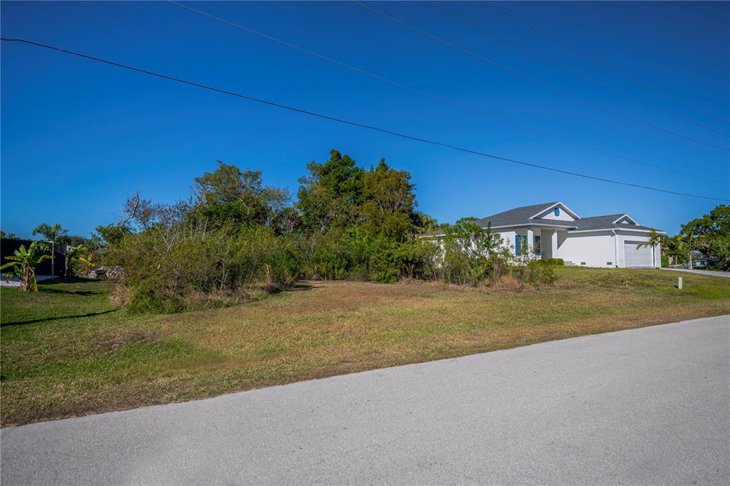 A vacant, grassy lot sits next to a white single-story house under a clear sky — 3013 CHAPMAN BOULEVARD, PUNTA GORDA, FL