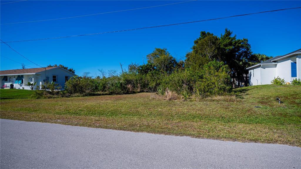 A vacant, grassy residential lot sits between two houses under a clear blue sky — 3013 CHAPMAN BOULEVARD, PUNTA GORDA, FL