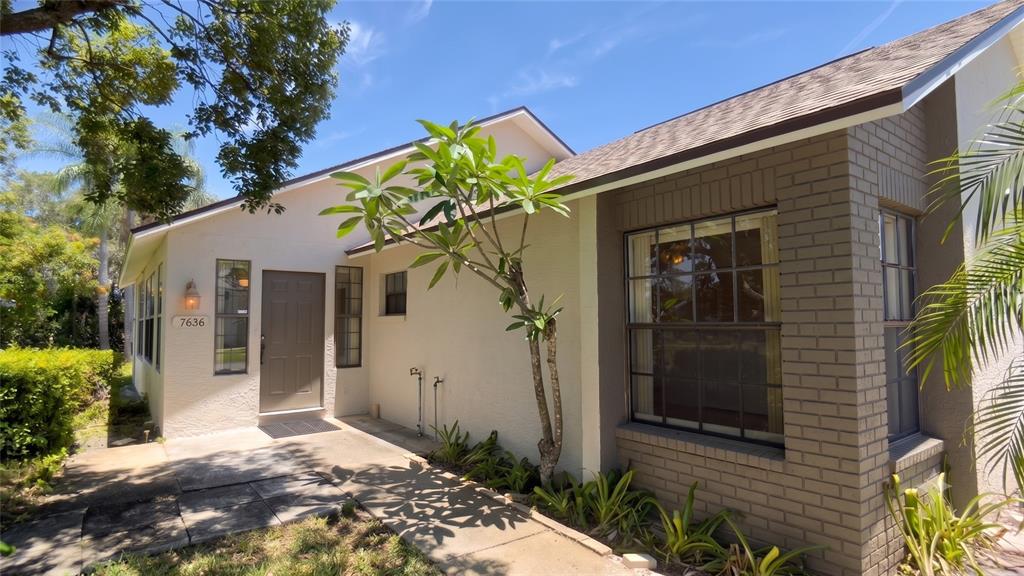 The exterior of a house features a tan stucco wall, a brick corner, and a front door — 7636 HAIG COURT, NEW PORT RICHEY, FL