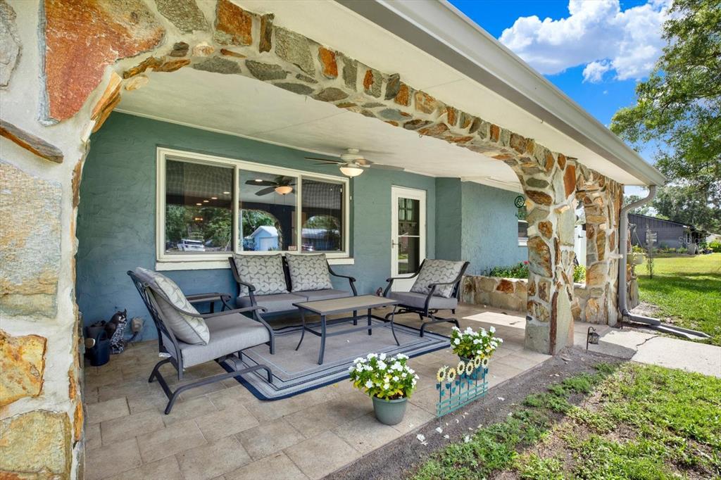 A covered stone-arched patio features outdoor furniture, a rug, and potted flowers on a paved floor — 11519 BELMACK BOULEVARD N, ODESSA, FL