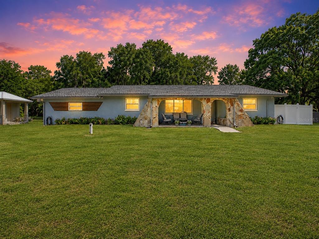 A single-story house with a stone-accented porch sits on a large lawn at sunset — 11519 BELMACK BOULEVARD N, ODESSA, FL
