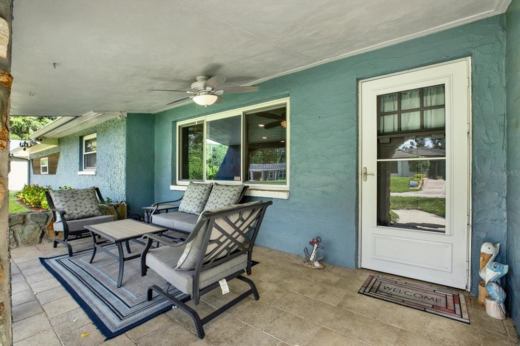 A covered porch features blue stucco walls, tiled flooring, outdoor furniture, and a white door — 11519 BELMACK BOULEVARD N, ODESSA, FL