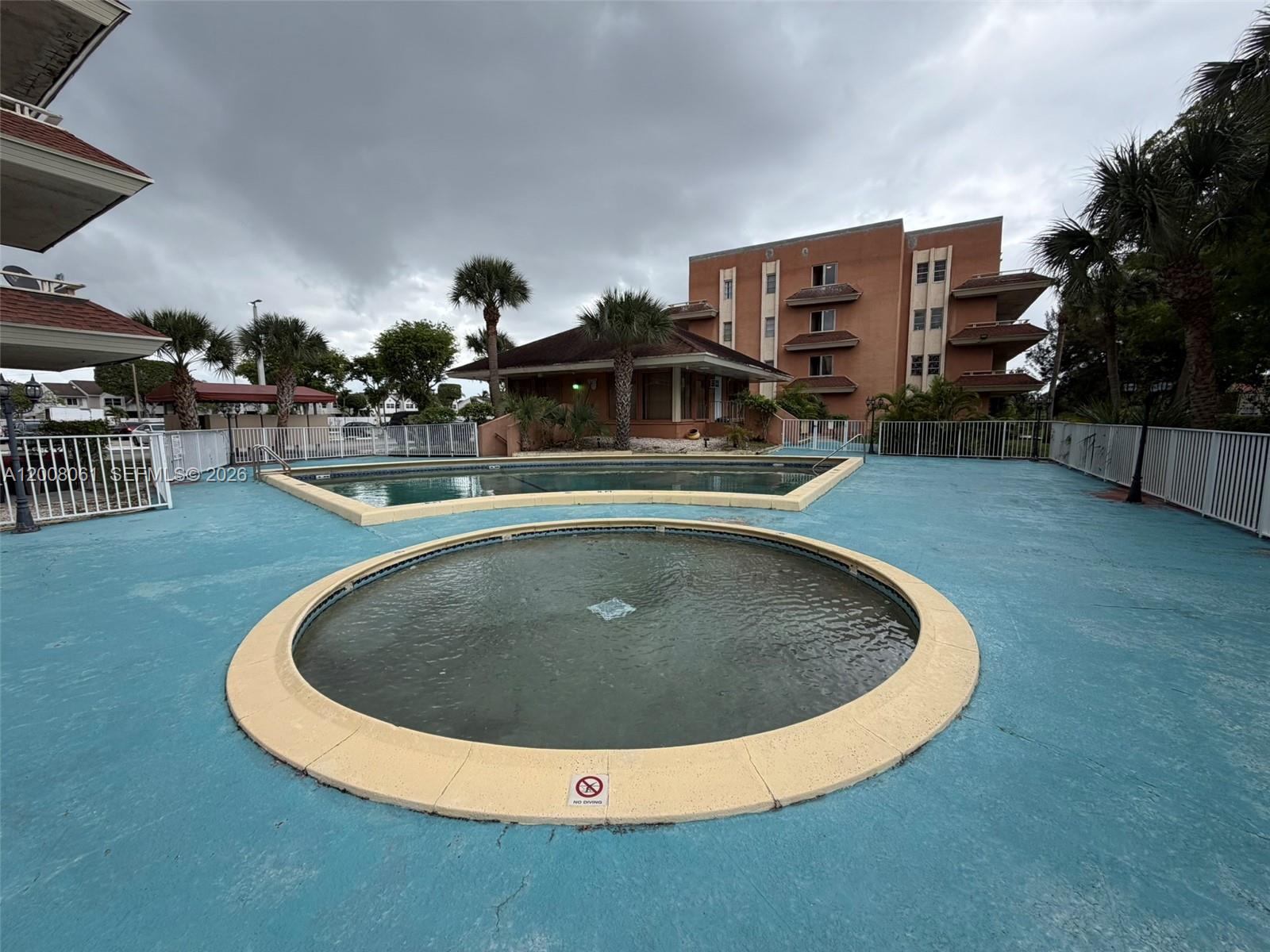 An outdoor pool area features a circular hot tub and a larger pool with blue decking — 17650 NW 68th Ave # A2008, Hialeah FL 33015, HIALEAH, FL