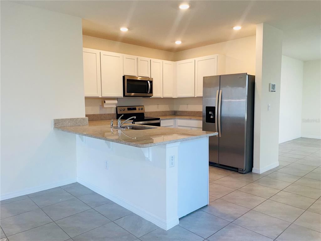 A kitchen with white cabinets, stainless steel appliances, and a granite-topped breakfast bar — 17043 OVAL RUM DRIVE, WIMAUMA, FL