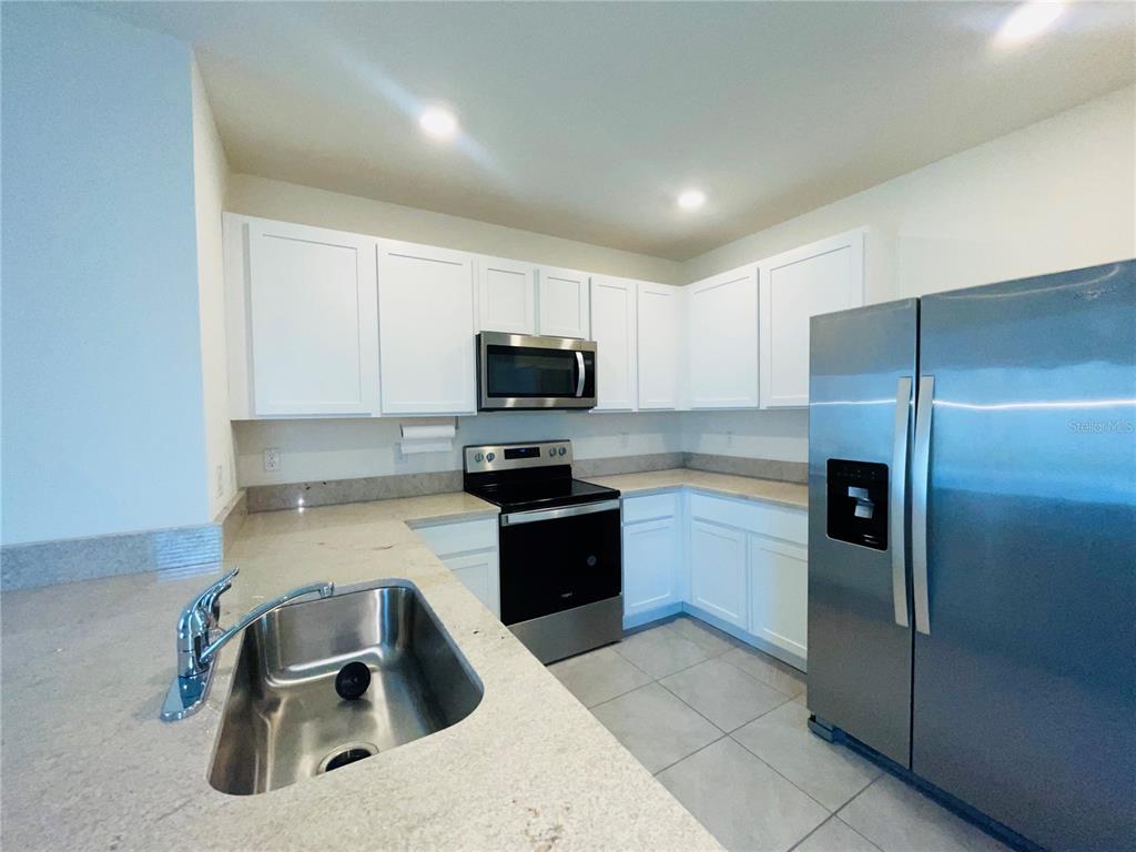 A kitchen features white cabinets, stainless steel appliances, a double-basin sink, and light countertops — 17043 OVAL RUM DRIVE, WIMAUMA, FL