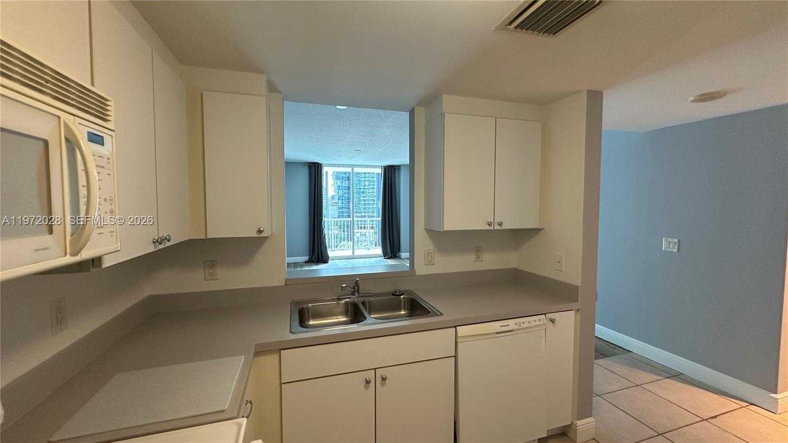 A kitchen features white cabinets, a double sink, and a pass-through window to the living area — 1250 S Miami Ave # 1012, Miami FL 33130, MIAMI, FL
