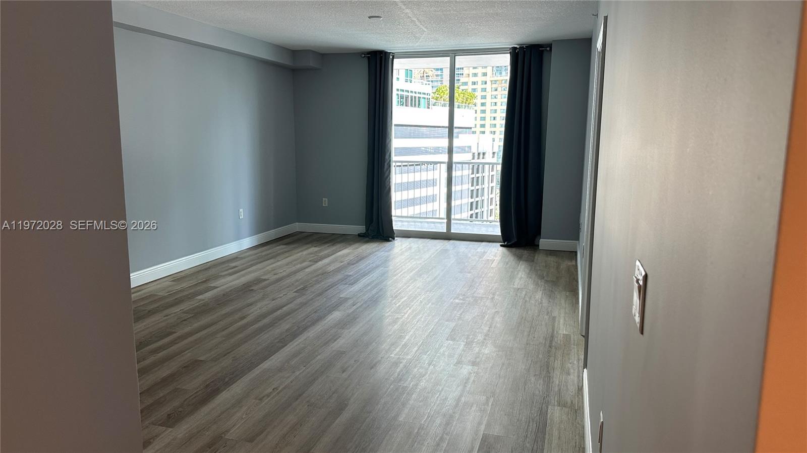 An empty room features gray walls, wood-look flooring, and a sliding glass door with curtains — 1250 S Miami Ave # 1012, Miami FL 33130, MIAMI, FL