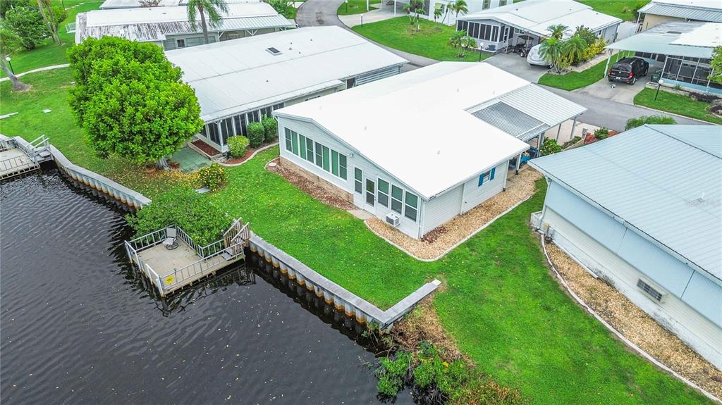 An aerial view shows a waterfront mobile home with a private dock and metal roof — 162 BERMUDA WAY, NORTH PORT, FL