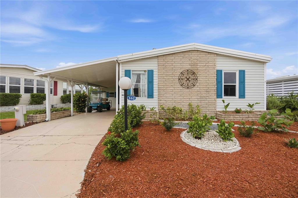 A single-story manufactured home features a brick facade, blue shutters, and a covered carport — 162 BERMUDA WAY, NORTH PORT, FL