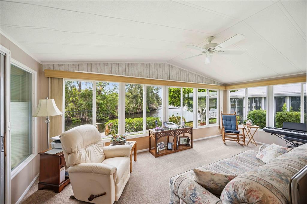 A sunroom with carpeted floors, a ceiling fan, and large windows overlooking a canal — 162 BERMUDA WAY, NORTH PORT, FL