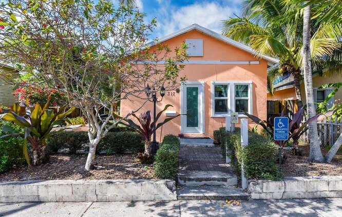 A single-story peach-colored house with a front walkway, a small tree, and a handicap sign — 317 N D Street E, FL 33460, FL