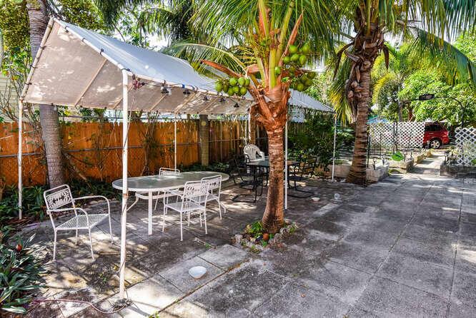 A patio area features a white canopy, a glass-topped table, chairs, and a coconut palm tree — 317 N D Street E, FL 33460, FL