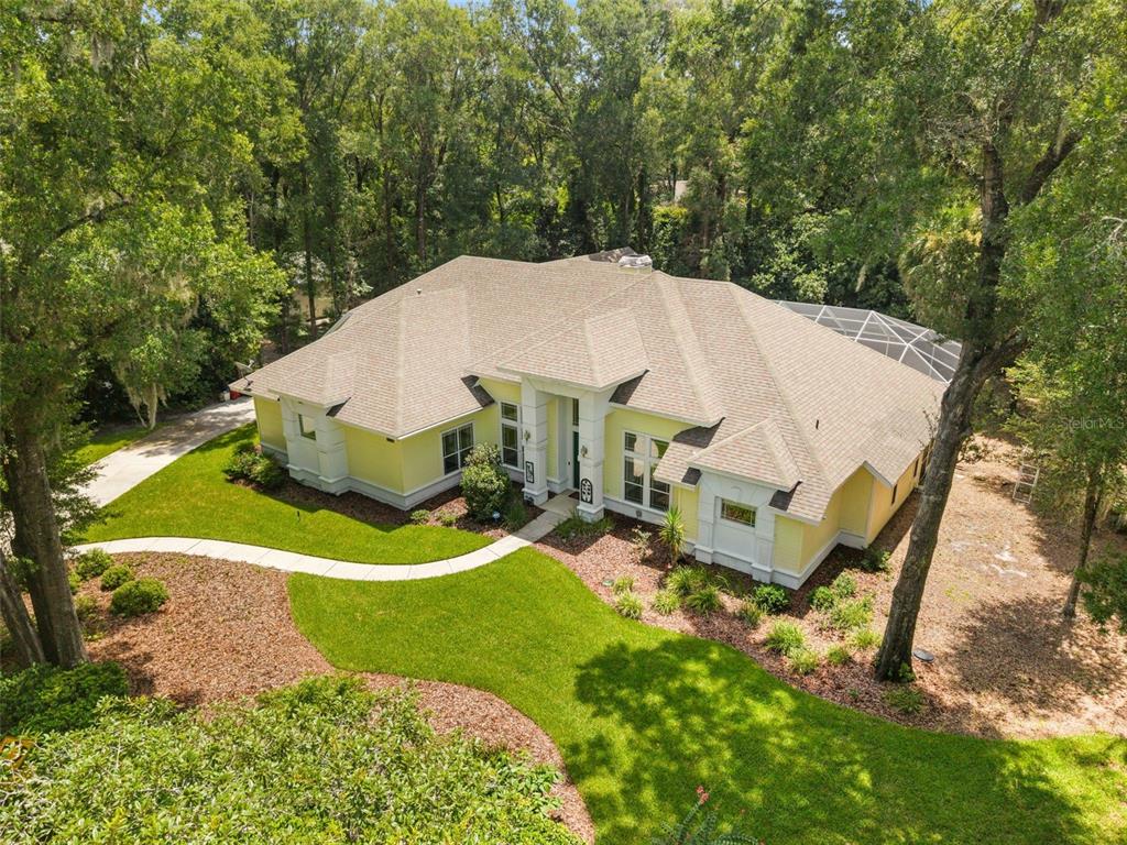 A yellow single-story house with a concrete driveway and surrounding trees under a blue sky — 9627 SW 40TH LANE, GAINESVILLE, FL