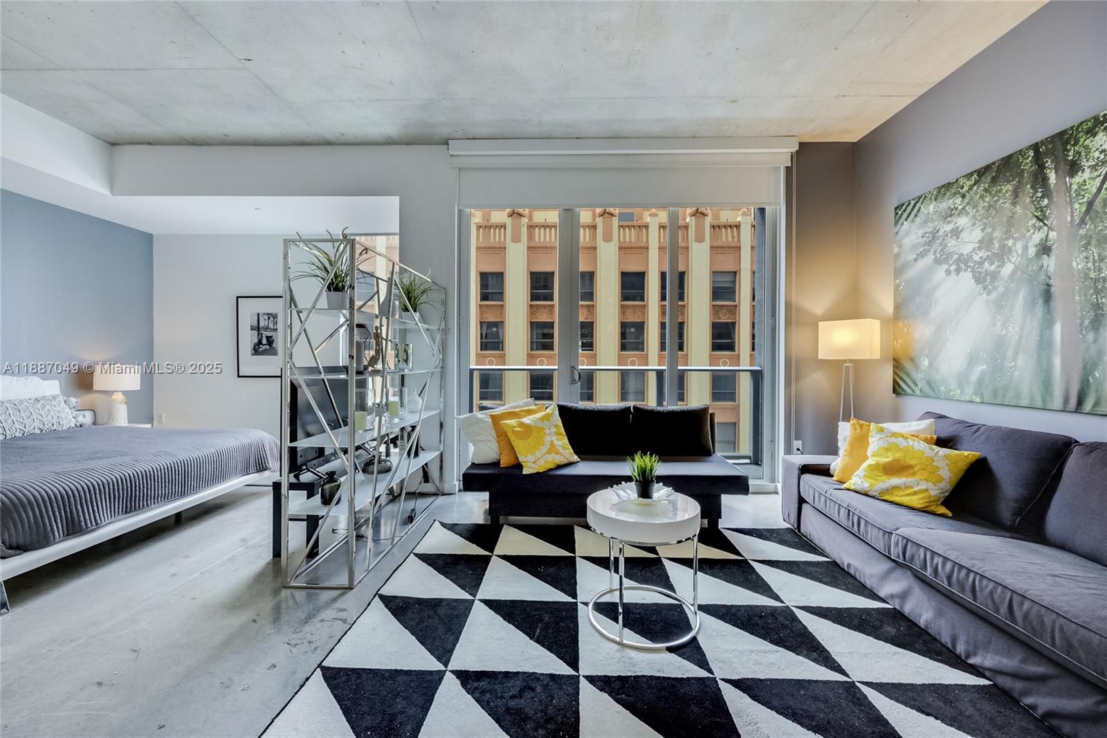 A modern living room and bedroom area with concrete ceilings, a geometric rug, and balcony — 151 SE 1st St # 1003, Miami FL 33131, MIAMI, FL