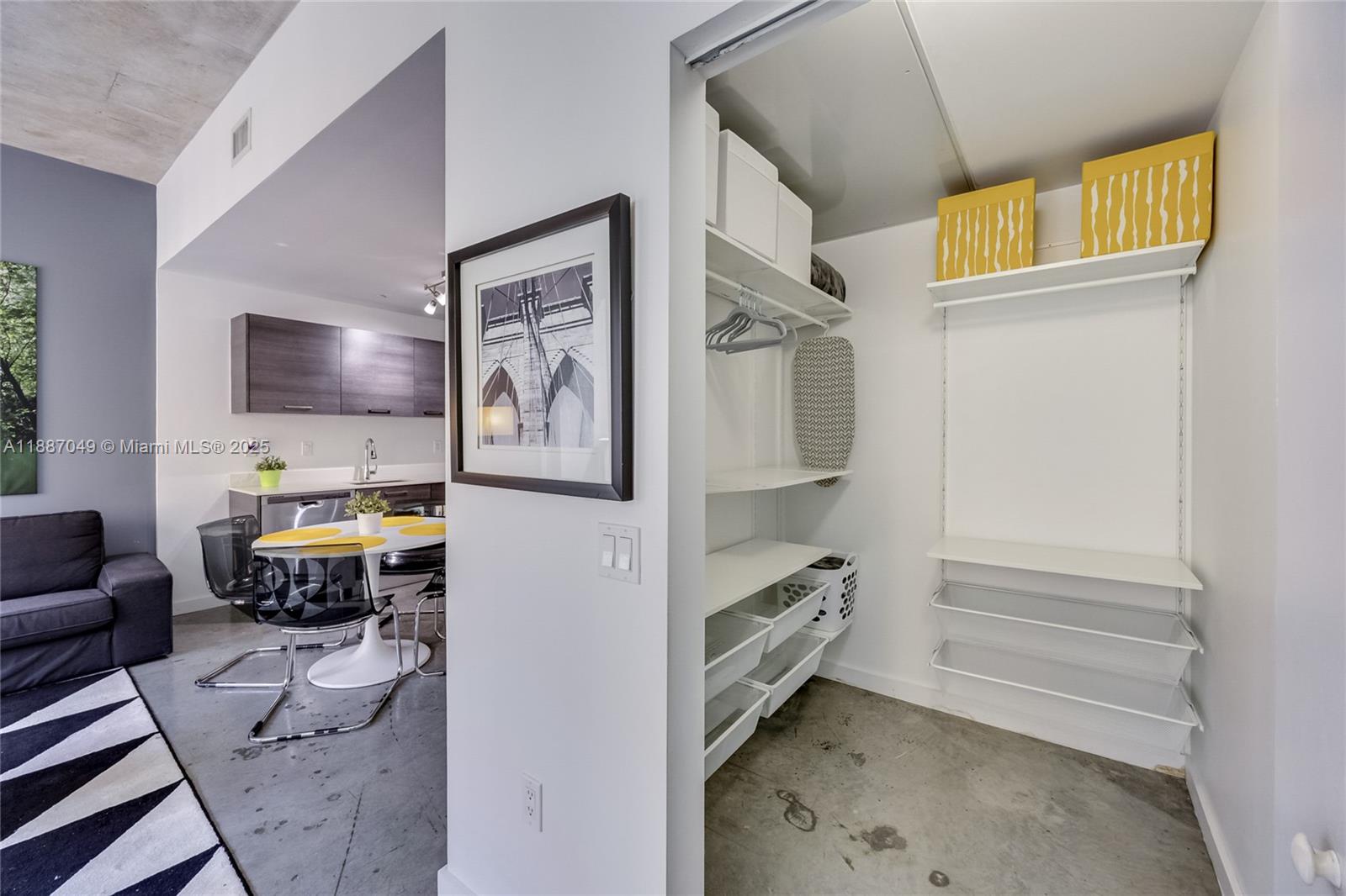 A closet with white shelving and storage bins sits next to a modern dining area — 151 SE 1st St # 1003, Miami FL 33131, MIAMI, FL