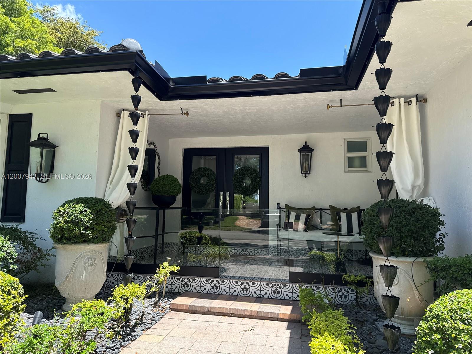 A white house exterior features a glass-enclosed porch with decorative tile and rain chains — 16241 W Troon Cir, Miami Lakes FL 33014, MIAMI LAKES, FL