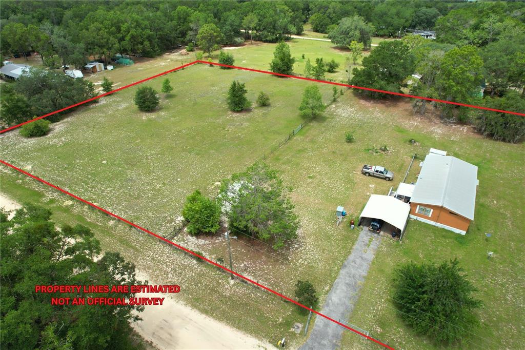 An aerial view shows a house with a carport on a large, fenced grassy lot — 107 GREEN OAK DRIVE, MELROSE, FL