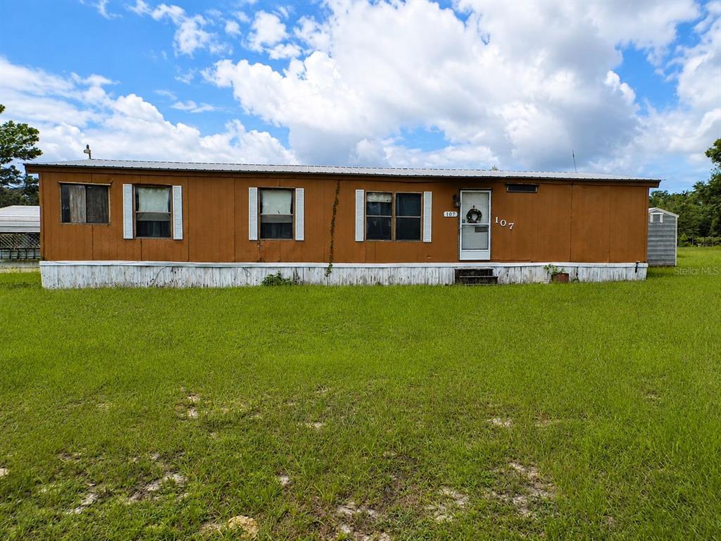 A single-story brown mobile home sits on a grassy lot under a cloudy sky — 107 GREEN OAK DRIVE, MELROSE, FL