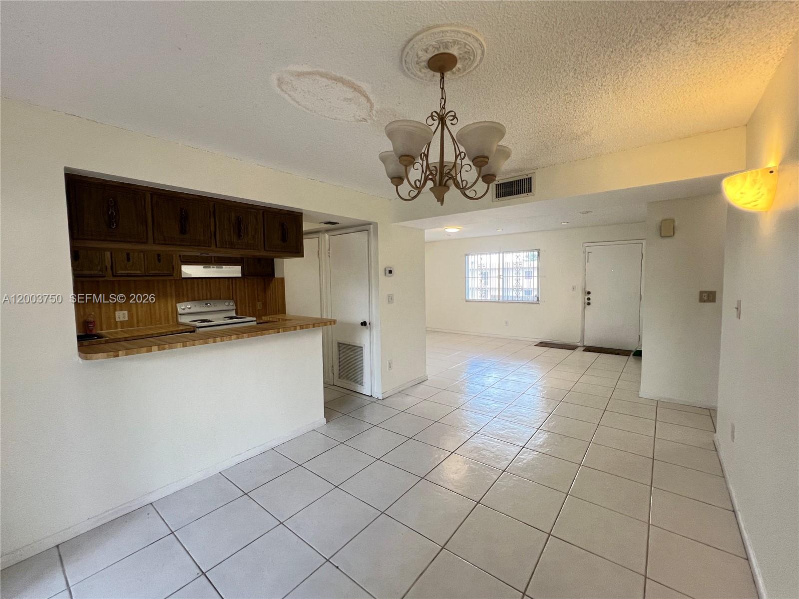 An open-concept kitchen and living area features white tile flooring and a central chandelier — 8401 SW 107th Ave # 322E, Miami FL 33173, MIAMI, FL