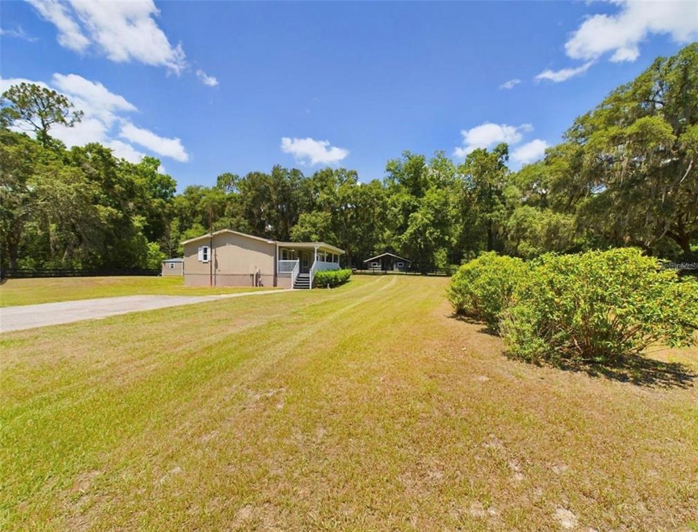 A single-story house with a porch sits on a large, grassy lot with trees — 12250 NW 7TH PLACE, OCALA, FL