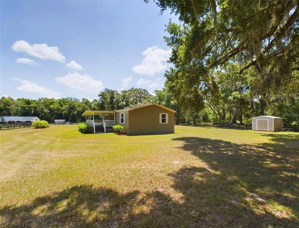 A tan mobile home with a covered porch sits on a large, grassy, fenced lot — 12250 NW 7TH PLACE, OCALA, FL