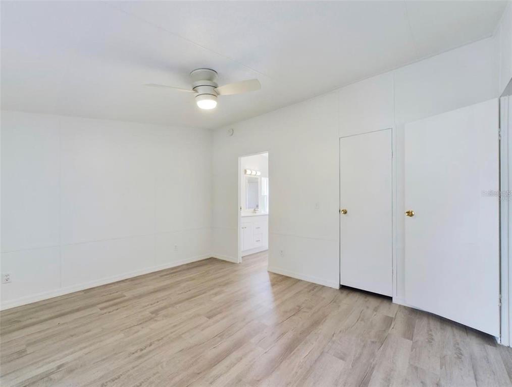 A bedroom with white walls, light wood-look flooring, a ceiling fan, and two closed doors — 12250 NW 7TH PLACE, OCALA, FL