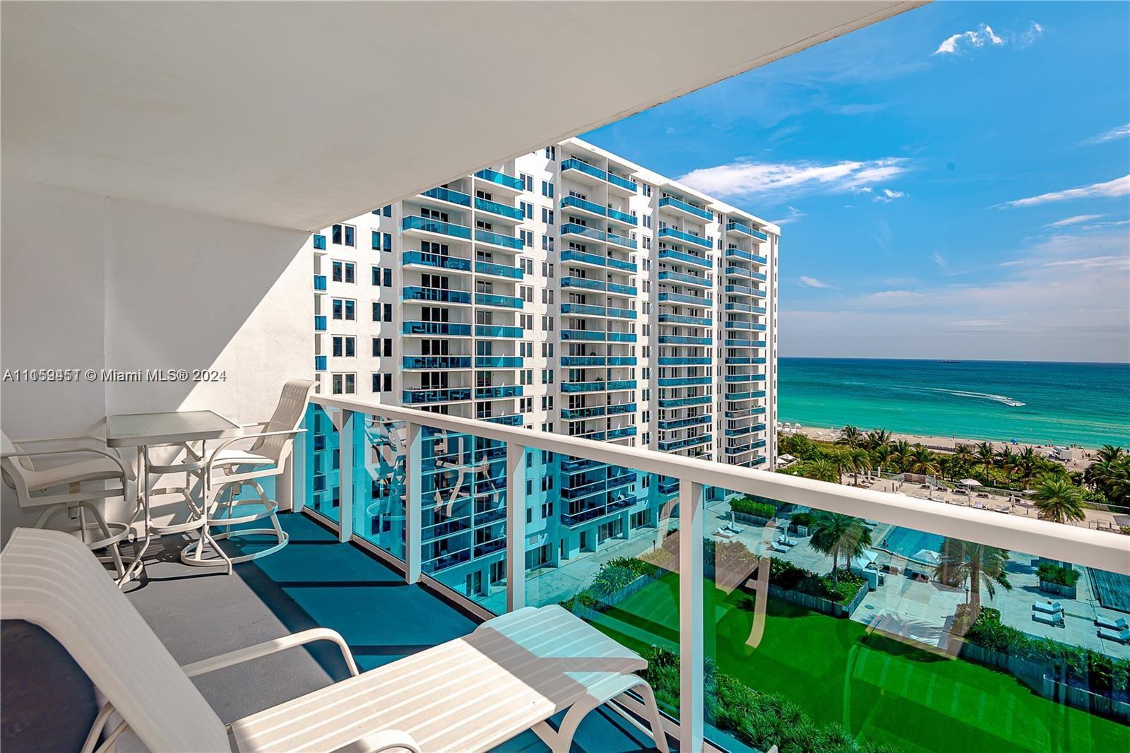 A balcony with patio furniture overlooks a large residential building, swimming pool, and the ocean — 2301 Collins Ave # 938, Miami Beach FL 33139, MIAMI BEACH, FL