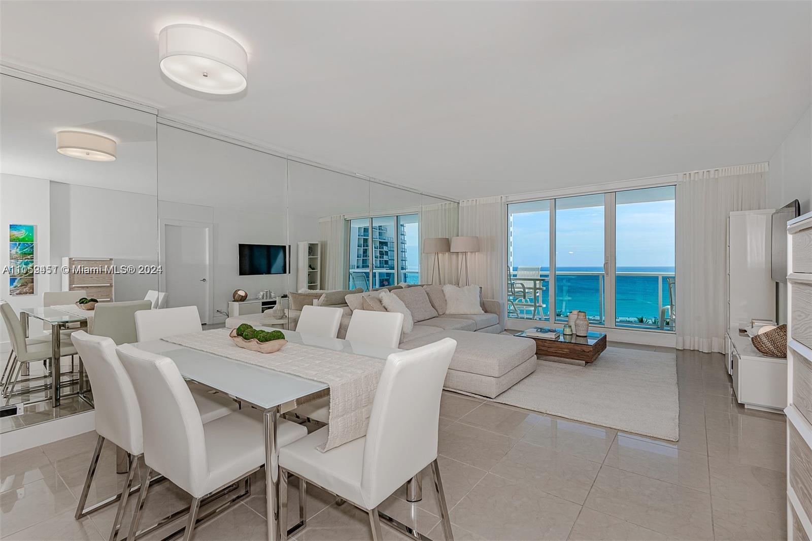 A bright, open-concept living and dining area features white furniture, mirrored walls, and ocean views — 2301 Collins Ave # 938, Miami Beach FL 33139, MIAMI BEACH, FL