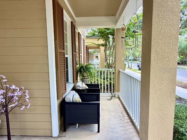 A covered front porch features tan siding, brown shutters, a dark chair, and a white railing — 10378 LAKE DISTRICT LANE UNIT 2B, ORLANDO, FL