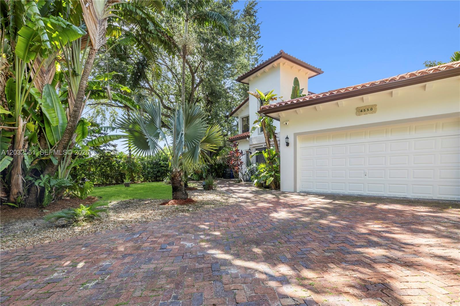 A brick driveway leads to a white house with a garage and tropical landscaping — 6550 SW 75th Ter, South Miami FL 33143, SOUTH MIAMI, FL