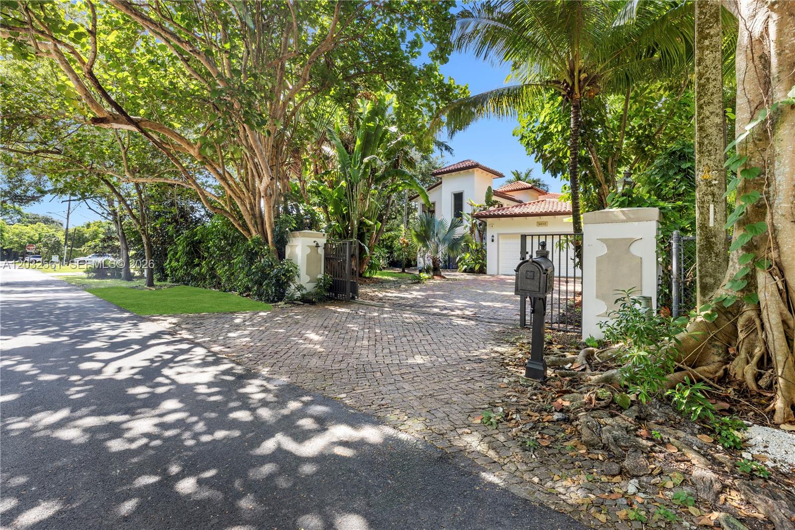 A paved driveway leads through a gated entrance to a two-story house with palm trees — 6550 SW 75th Ter, South Miami FL 33143, SOUTH MIAMI, FL