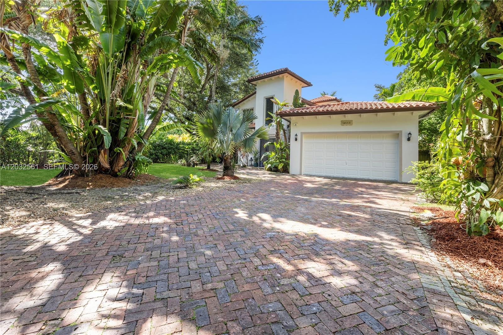 A two-story house with a brick driveway, a white garage, and lush tropical landscaping — 6550 SW 75th Ter, South Miami FL 33143, SOUTH MIAMI, FL