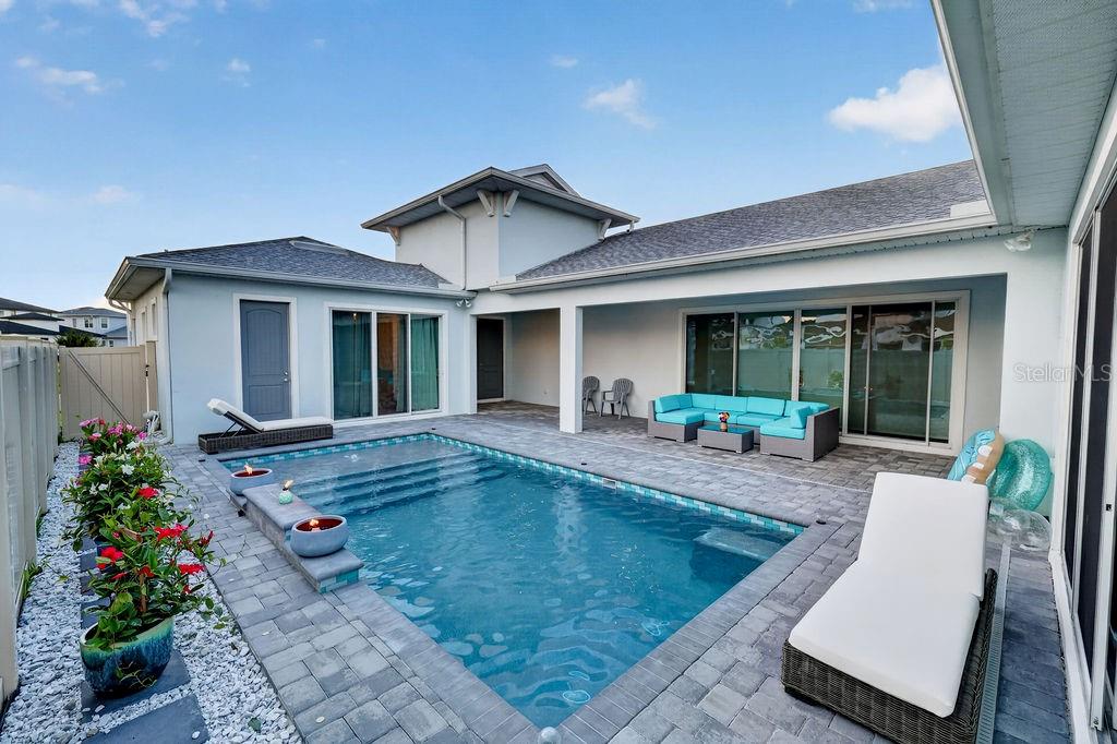 A backyard features a rectangular swimming pool, a paved patio, and a blue sectional sofa — 10470 PURPLE THISTLE WAY, SAN ANTONIO, FL