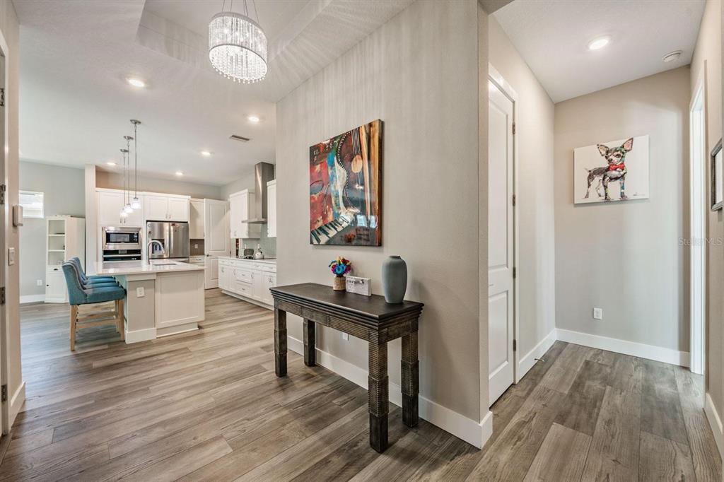 A foyer with a console table and abstract art leads into an open-concept white kitchen — 10470 PURPLE THISTLE WAY, SAN ANTONIO, FL