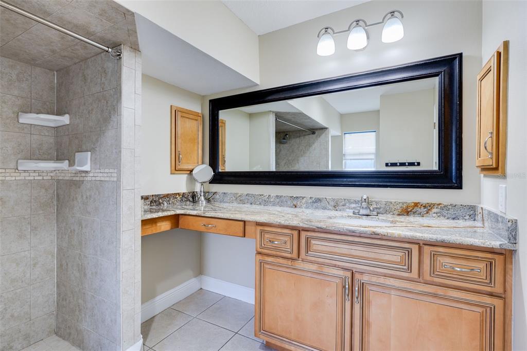 A bathroom vanity with a granite countertop, wooden cabinets, and a large black-framed mirror — 23230 GOLDCOAST AVENUE, PUNTA GORDA, FL