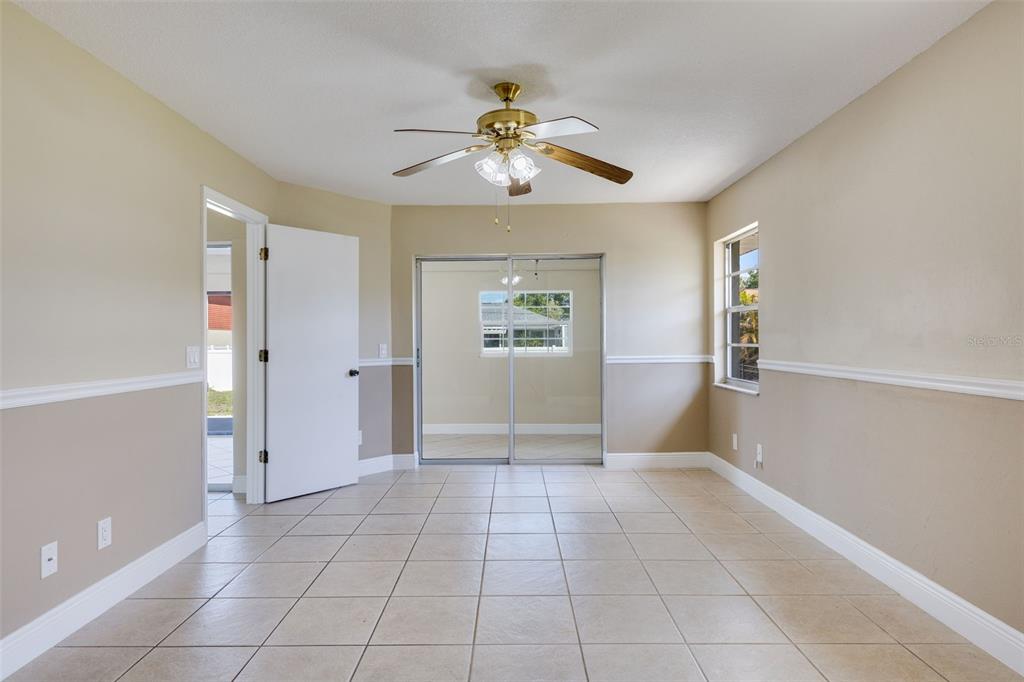 A bedroom with beige walls, white trim, tile flooring, a ceiling fan, and mirrored closet doors — 23230 GOLDCOAST AVENUE, PUNTA GORDA, FL