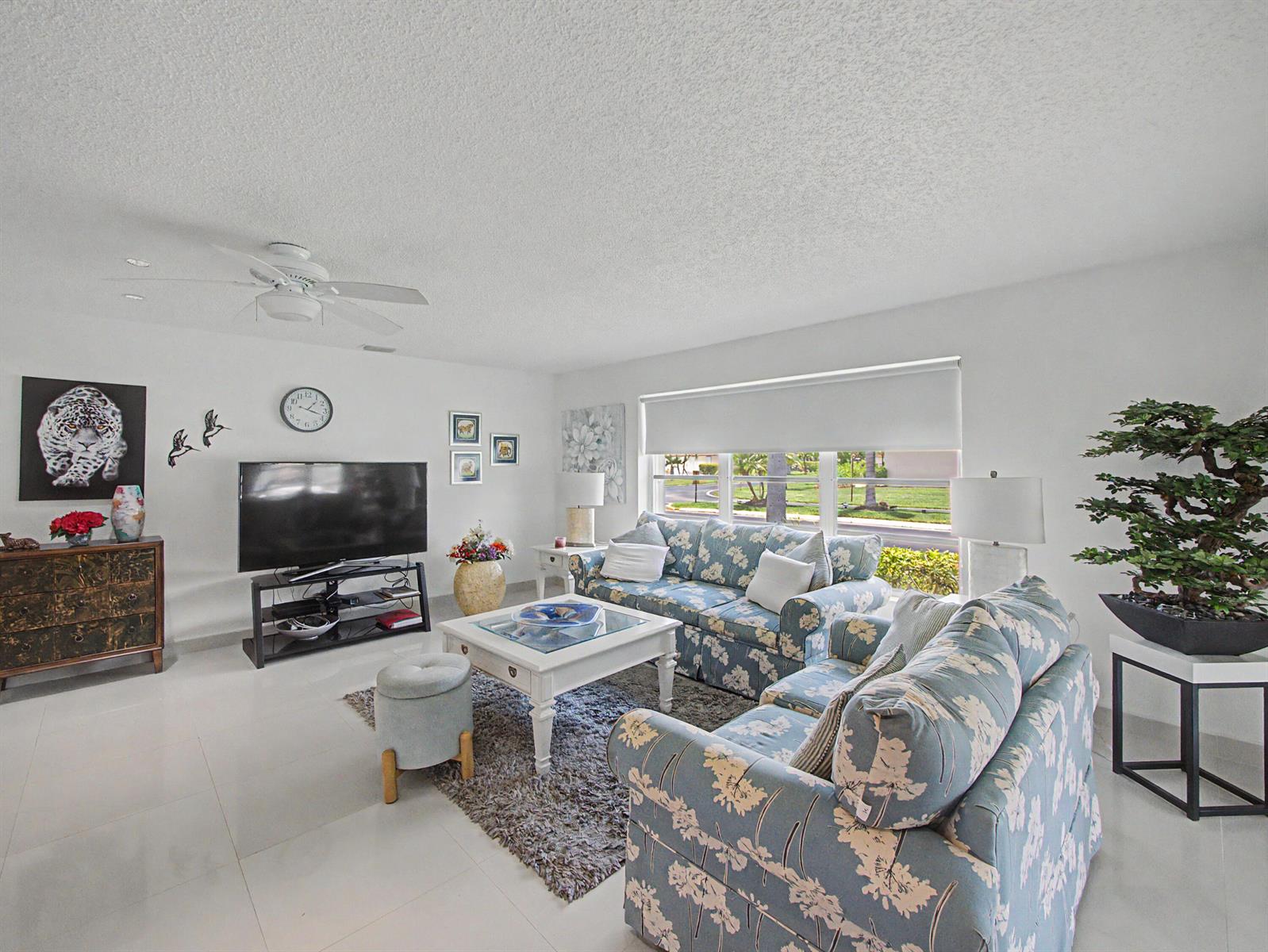 A living room features floral sofas, a white coffee table, a television, and a bonsai tree — 4580 NW 3rd Street # D, Delray Beach FL 33445, DELRAY BEACH, FL