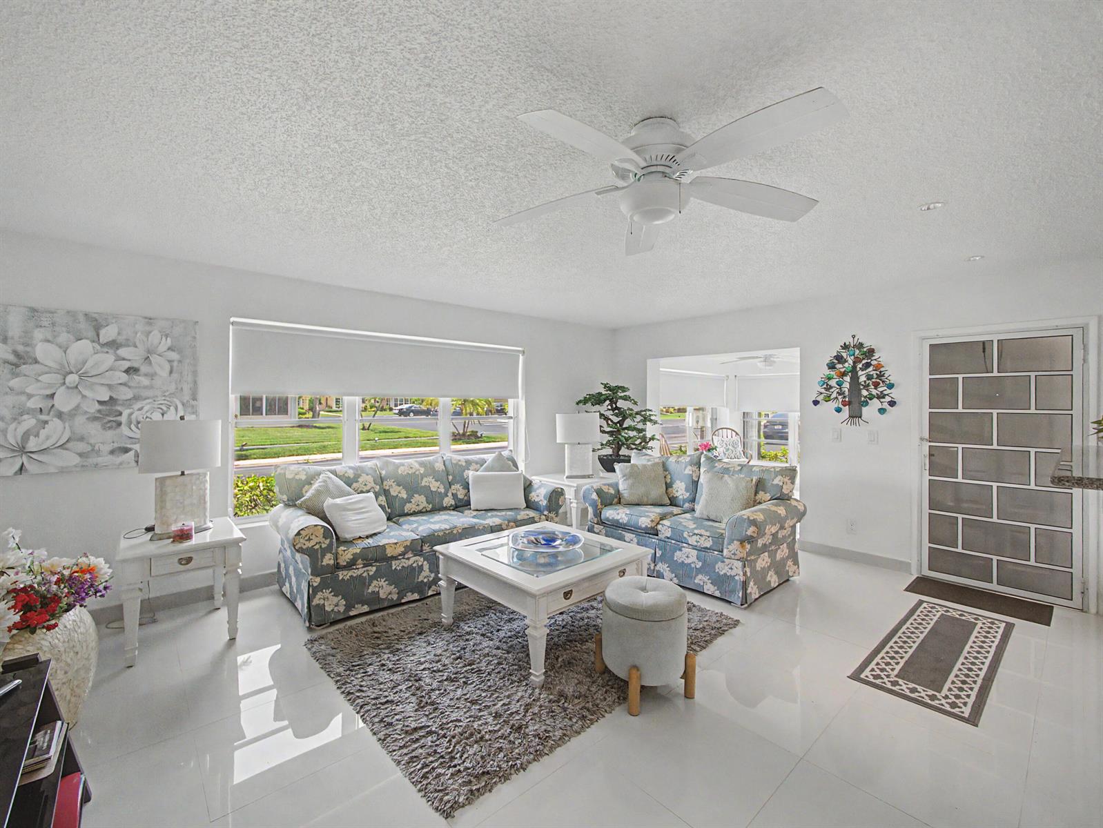 A bright living room features floral sofas, a white coffee table, and white tile flooring — 4580 NW 3rd Street # D, Delray Beach FL 33445, DELRAY BEACH, FL
