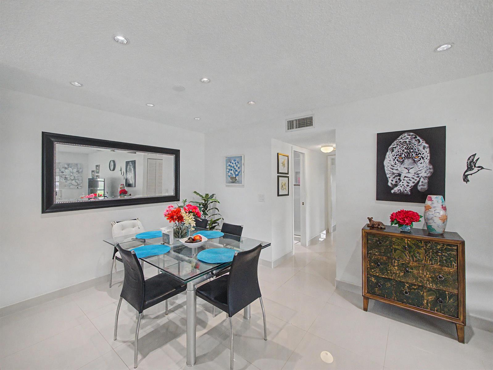 A dining room features a glass table, black chairs, a large mirror, and a decorative chest — 4580 NW 3rd Street # D, Delray Beach FL 33445, DELRAY BEACH, FL