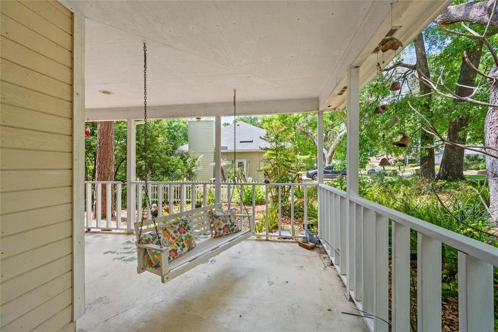 A covered porch features a white wooden swing, a railing, and views of surrounding trees — 2132 PALM VISTA DRIVE, APOPKA, FL