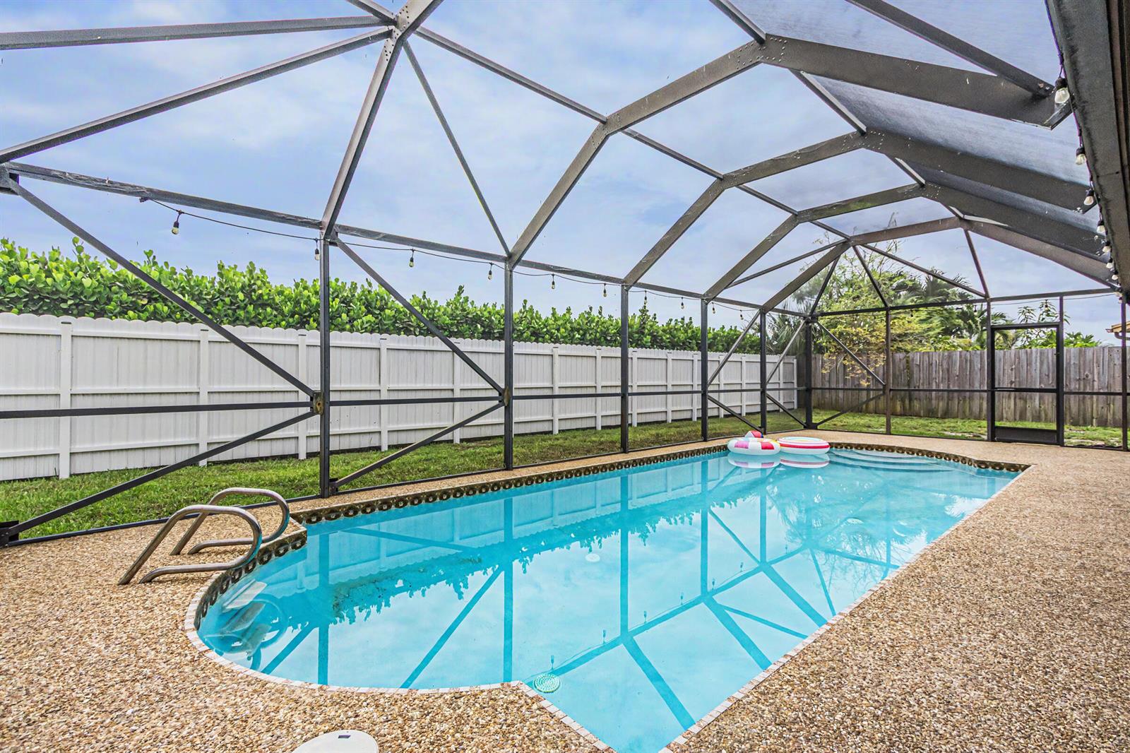 A swimming pool is enclosed by a screened lanai with a white vinyl fence behind — 630 NW 79th Avenue, Margate FL 33063, MARGATE, FL