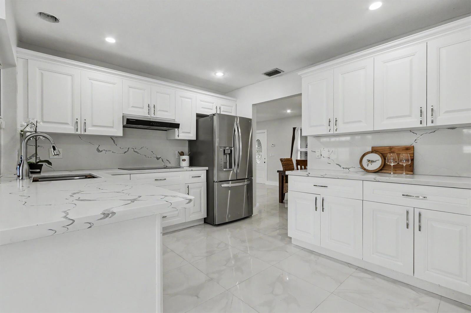 A modern kitchen features white cabinets, marble-patterned countertops, stainless steel appliances, and tile flooring — 630 NW 79th Avenue, Margate FL 33063, MARGATE, FL