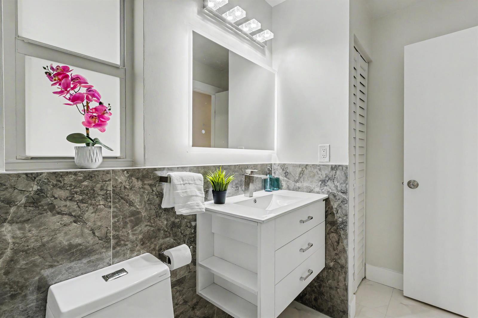 A bathroom features a white vanity, marble-look wall tiles, a backlit mirror, and a toilet — 630 NW 79th Avenue, Margate FL 33063, MARGATE, FL
